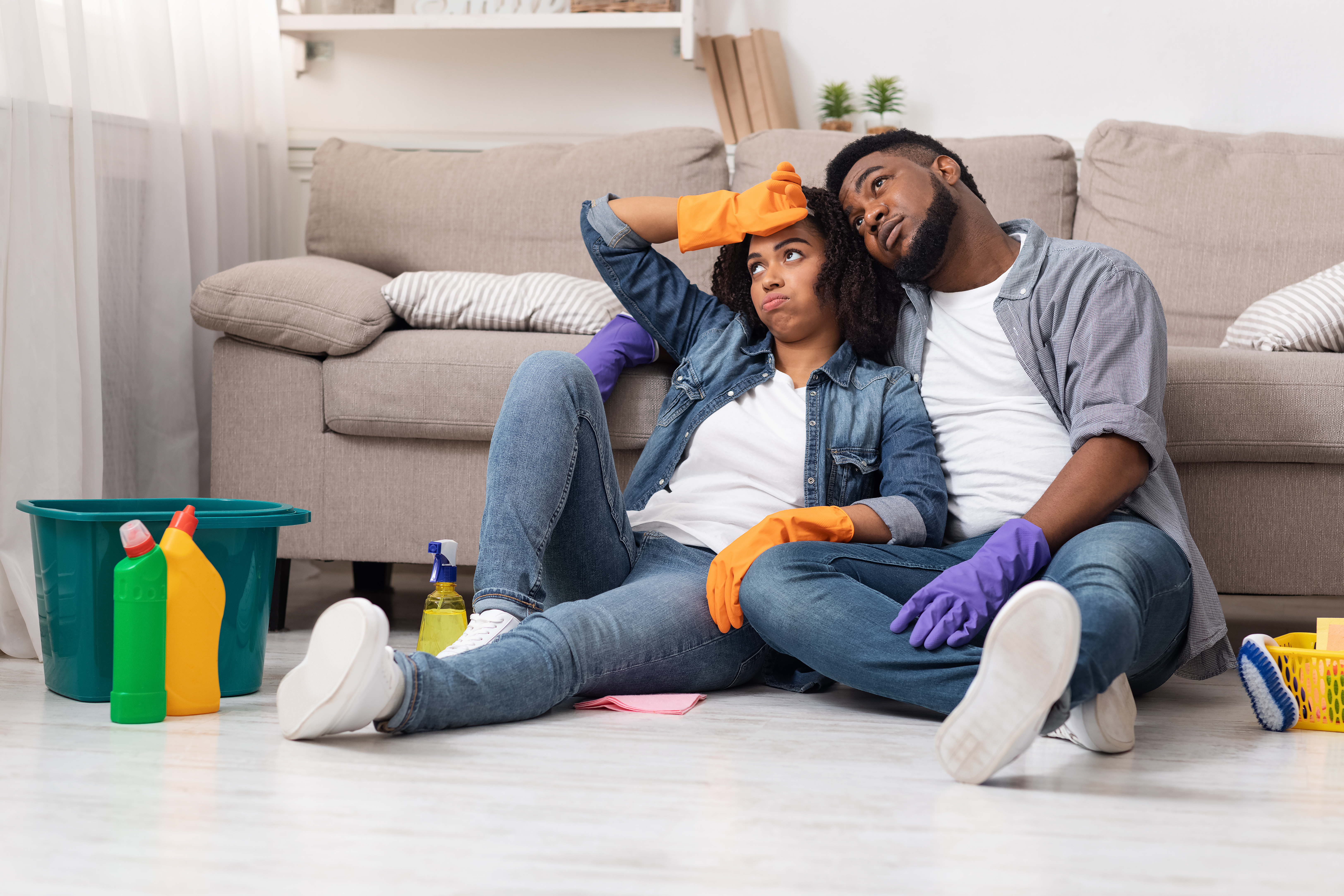 exhausted couple sitting on the floor surrounded by cleaning products and home improvement supplies