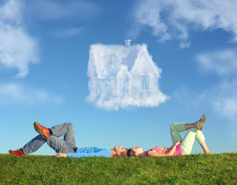 Couple lie on grass as a cloud forms a house over them