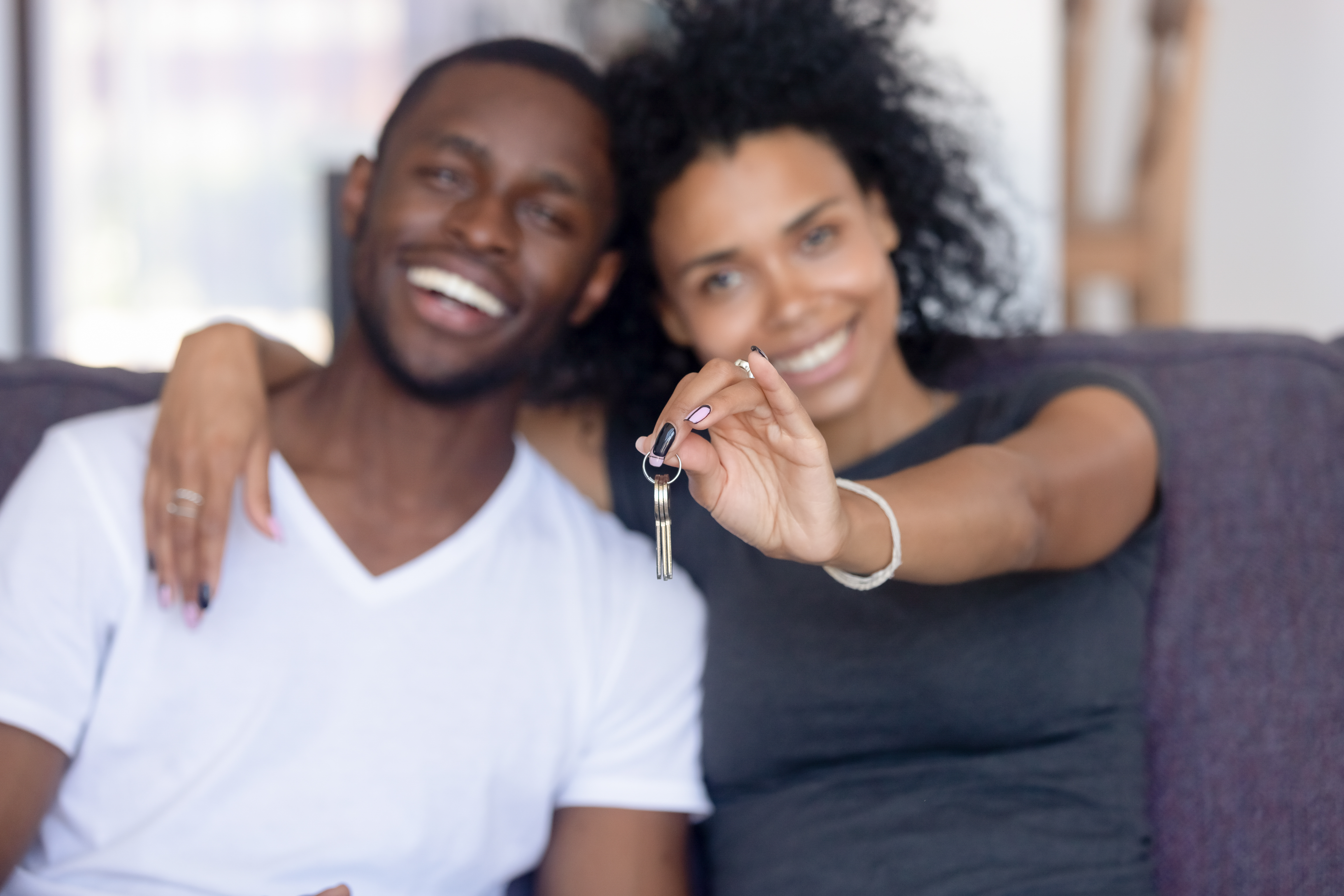 Excited young couple on sofa show keys to their new home.